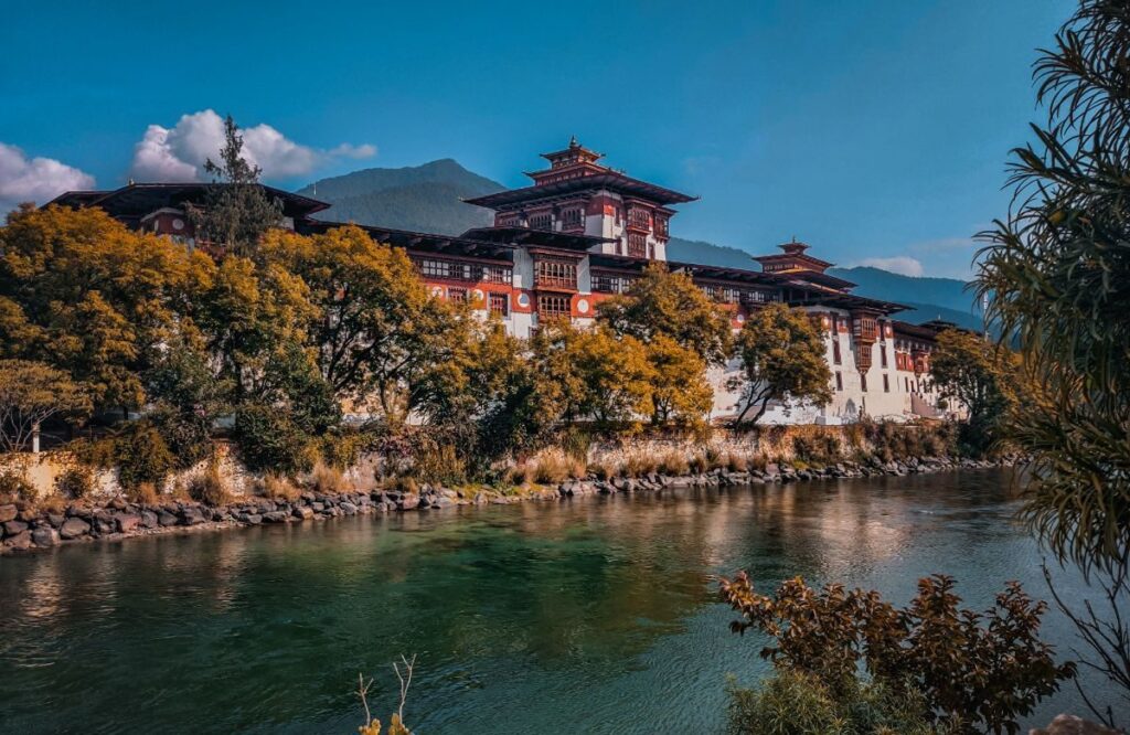 A dzong beside a green river with autumn trees along the bank