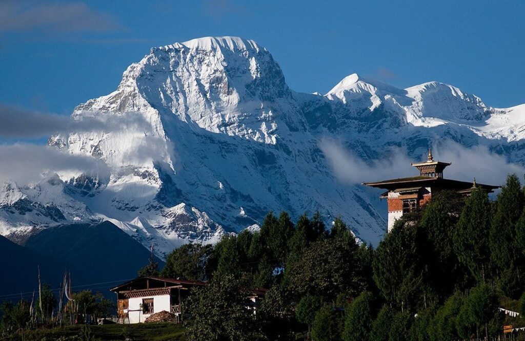 A snow-covered Himalayan peak rising behind a traditional Bhutanese farmhouse