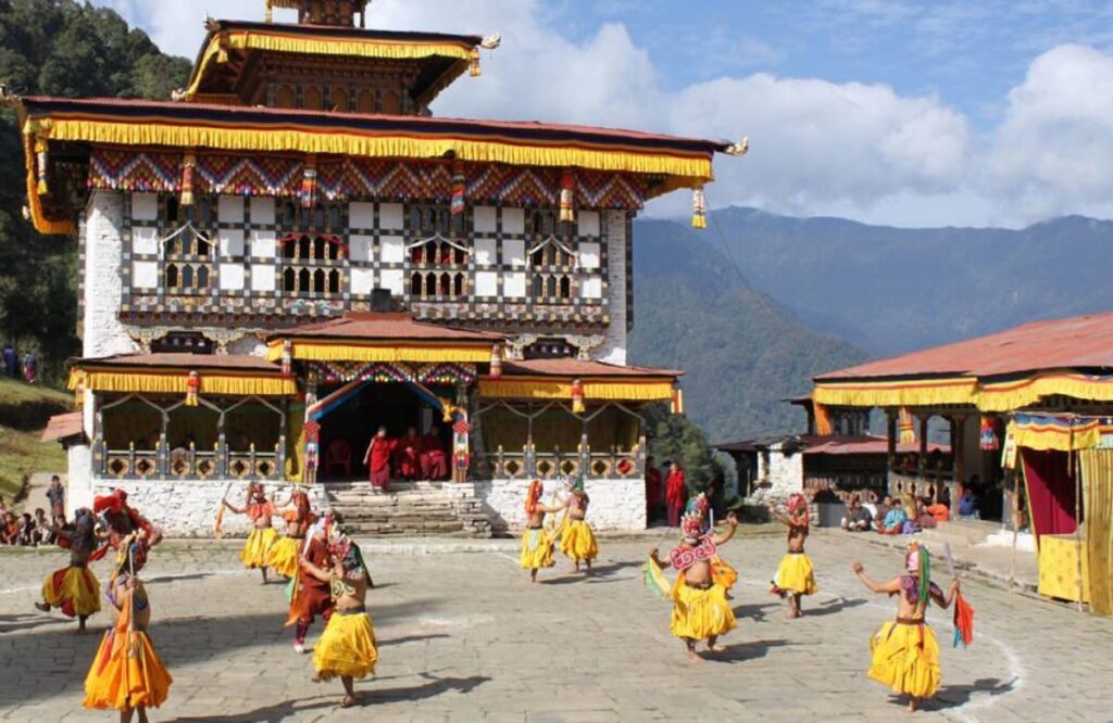 Masked dancers in yellow robes performing in a temple courtyard at a festival in the Haa valley, Bhutan