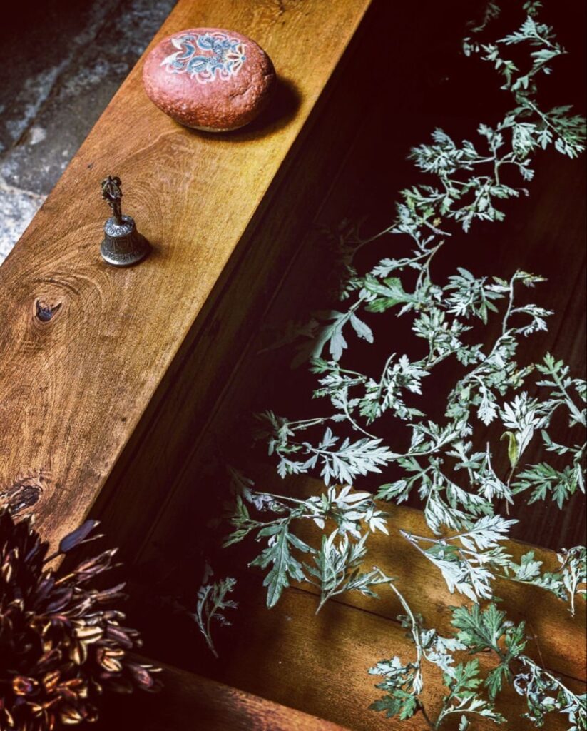 Fresh artemisia, a painted stone and a small ritual bell laid on a dark wooden table