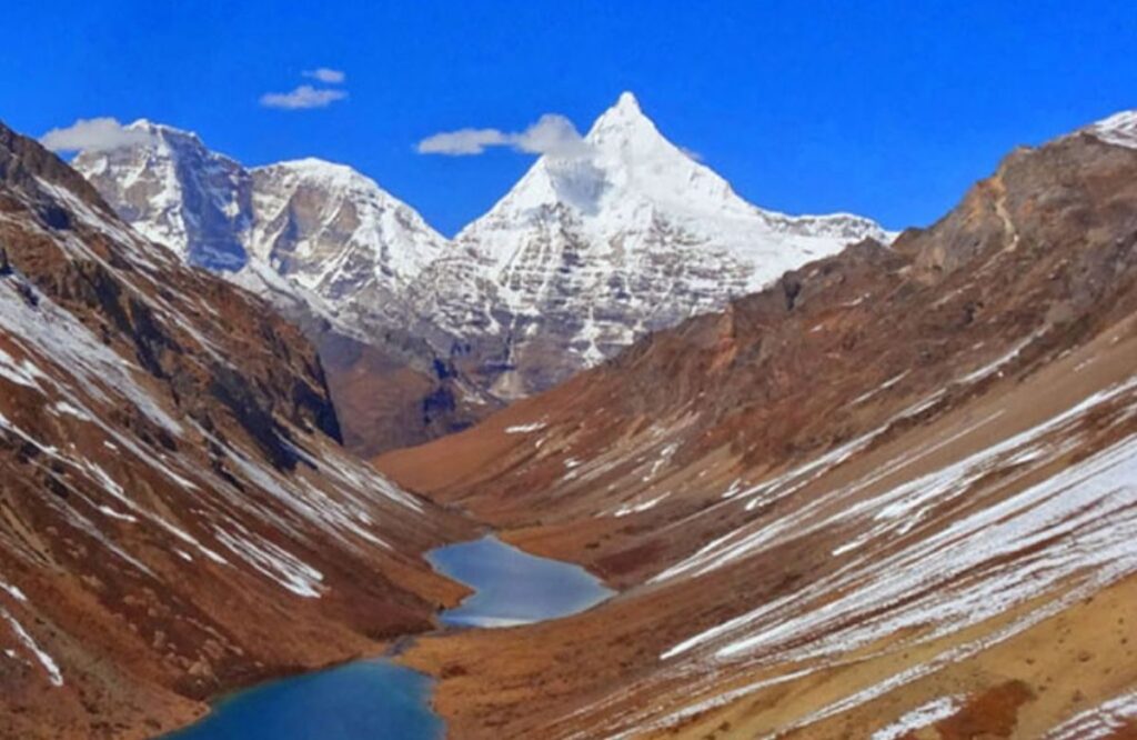 A turquoise lake in a high brown valley below a snow-covered peak