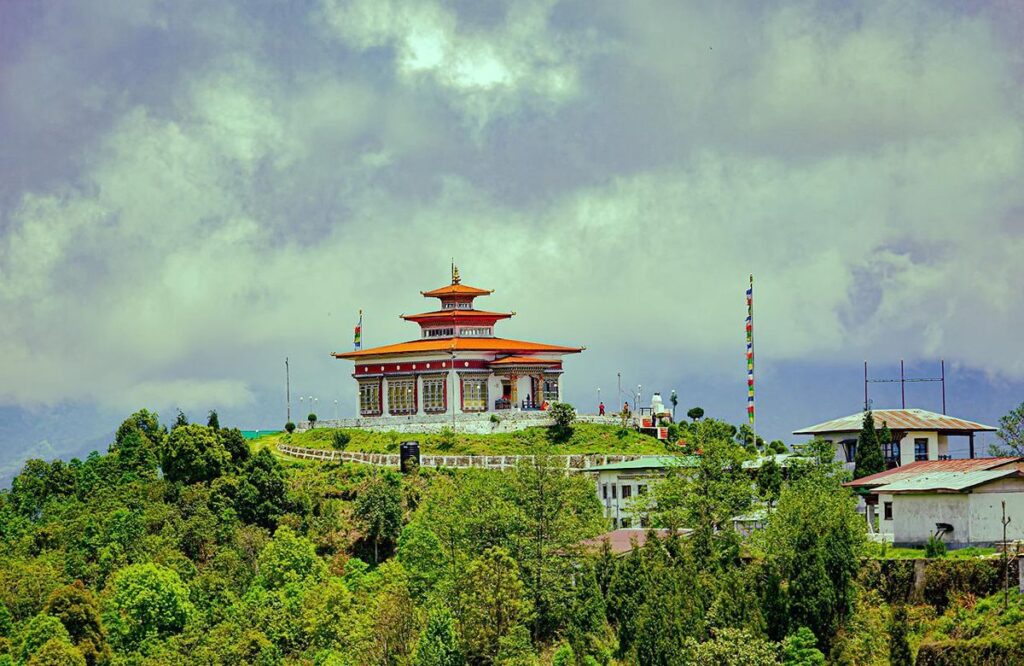 A temple with a golden roof on a green hilltop above wooded slopes
