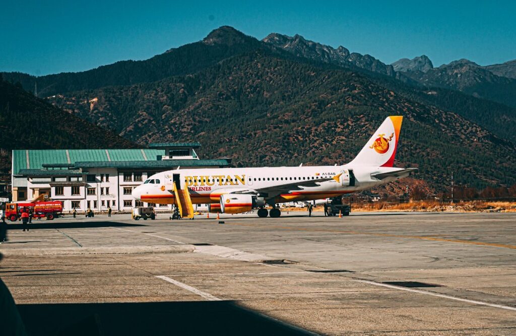 An airliner on the apron at Paro, the mountains rising directly behind the runway