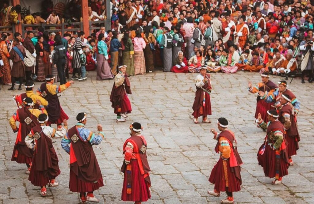 Dancers in dark robes circling in the courtyard before a seated crowd at Paro Tshechu
