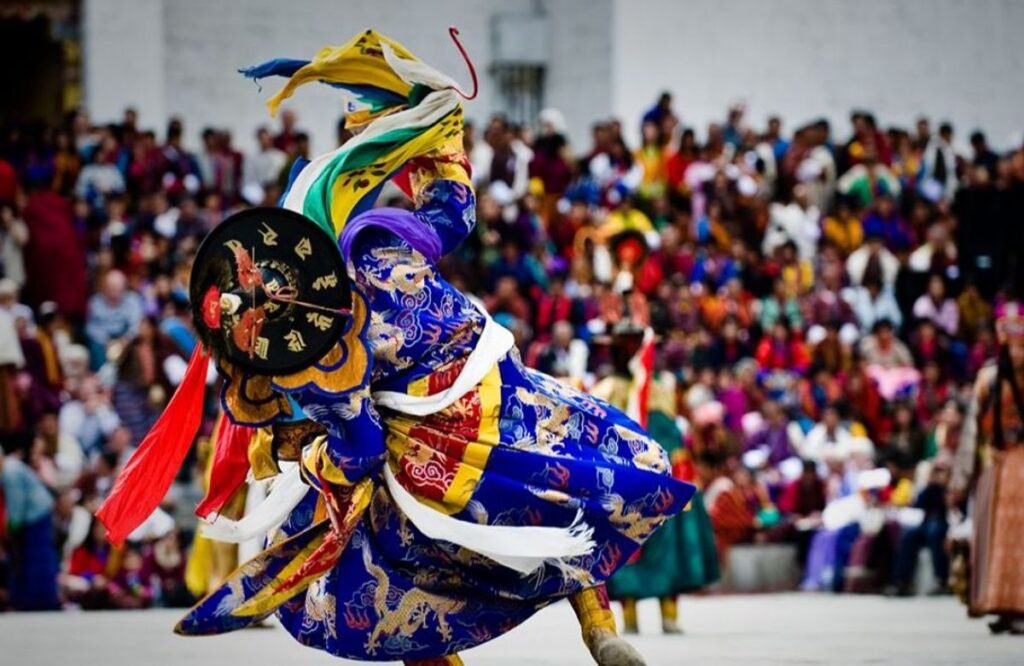 A dancer in a blue and gold mask performing before the crowd at Thimphu Tshechu