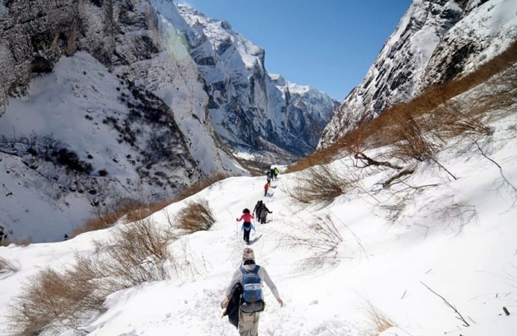 A line of trekkers crossing a snow slope below a rock face