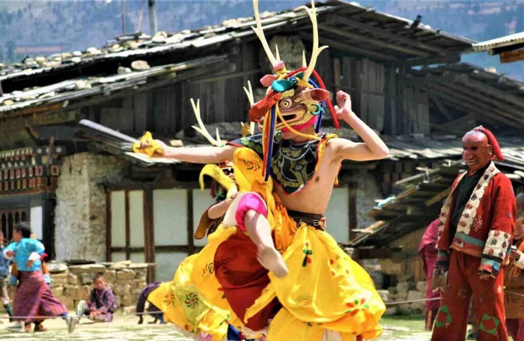 A masked dancer in a yellow silk robe mid-turn at the Ura Yakchoe festival in Bumthang
