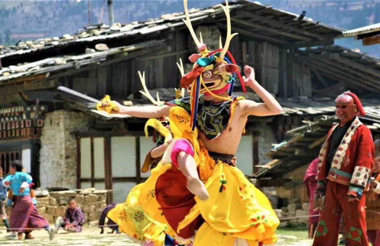 A masked dancer in a yellow silk robe mid-turn at the Ura Yakchoe festival in Bumthang