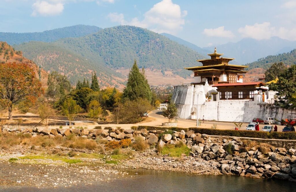 A white chorten on a stony riverbank with mountains behind